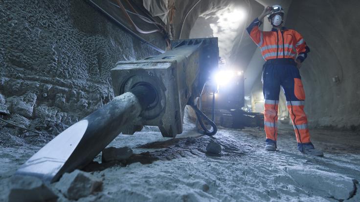 Photographer Samuel Hertzog, in an orange construction-site uniform, stands among heavy equipment in the tunnel
